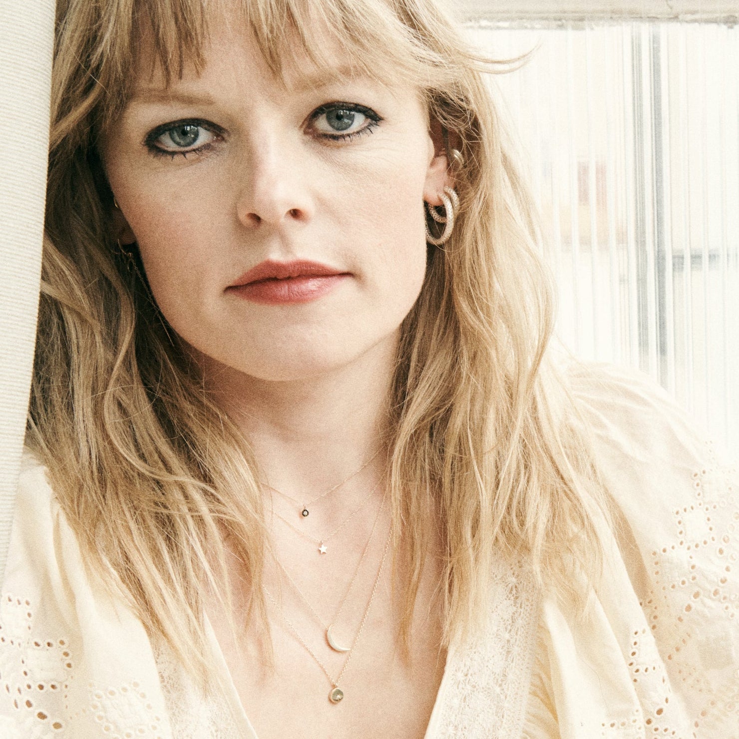 Woman with blonde hair and blue eyes wearing a light-colored top.