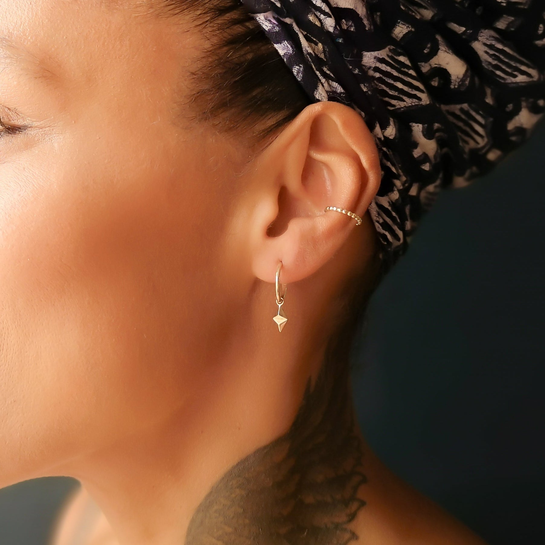 Close-up of a person wearing gold hoop earrings with pyramid charms attached